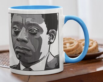 May include: White ceramic mug with a blue interior and handle. The mug features a black and white portrait of a man. The mug is sitting on a wooden table, with a plate of cookies in the background.