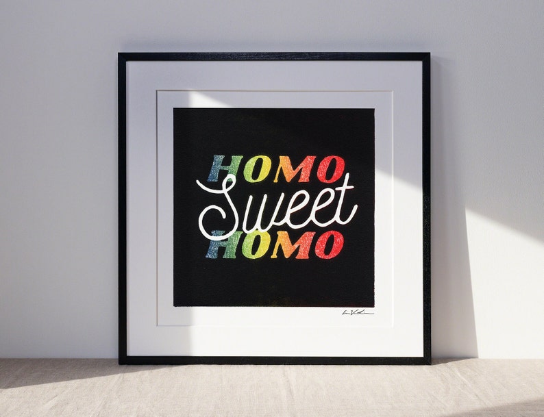 homo sweet homo linocut print in a black frame. the homo lettering is rainbow color while the SWEET is white allwitha black backdrop