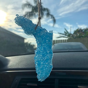 May include: A blue car air freshener shaped like the state of Florida, hanging from a rearview mirror in a car.