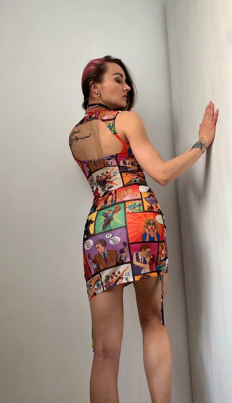 May include: A colorful, sleeveless mini dress featuring a comic book print. The dress has a high neckline, open back, and a fitted silhouette. The print includes various comic book panels with vibrant colors and bold graphics.