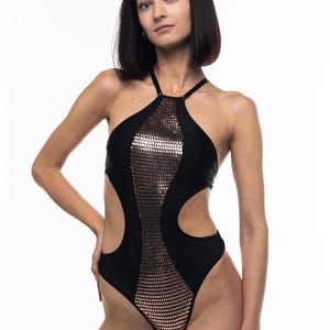 Puede incluir: Un bañador negro de una pieza con escote halter y recortes en los laterales. El bañador presenta un panel de lentejuelas en color oro rosa.