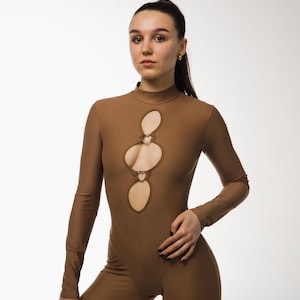 Può includere: Tuta marrone con maniche lunghe e collo alto. La tuta presenta tre ritagli a forma di cuore sul davanti. La modella è in piedi davanti a uno sfondo bianco.