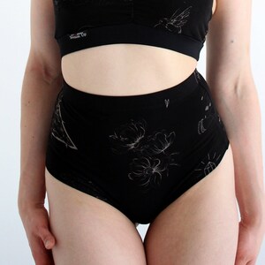 May include: Black high-waisted underwear with a floral and geometric print. The underwear has a wide waistband and a high leg cut. The text "Dream Up" is printed on the waistband.
