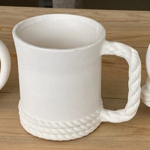 May include: White ceramic mug with a rope-like handle and a rope design around the bottom.