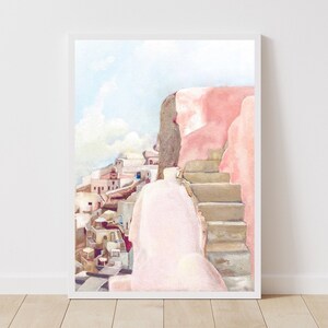 May include: A vertical watercolor painting in a white frame depicting a Mediterranean coastal scene with light pink walls, stone steps, and a cluster of white buildings under a pale blue sky. The artwork features soft pastel tones and architectural details.