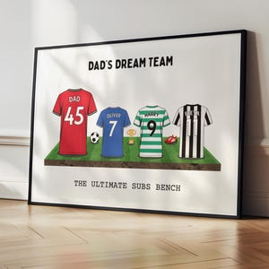 May include: Framed print featuring four soccer jerseys on a green field. The jerseys are red, blue, green, and black and white striped. Text at the top reads "DAD'S DREAM TEAM" and at the bottom "THE ULTIMATE SUBS BENCH".