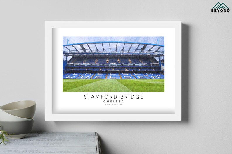 May include: A white framed print of Stamford Bridge, the home of Chelsea Football Club. The image shows the stadium's exterior with a blue and white color scheme. The text "Stamford Bridge, Chelsea, Opened in 1905" is printed below the image.