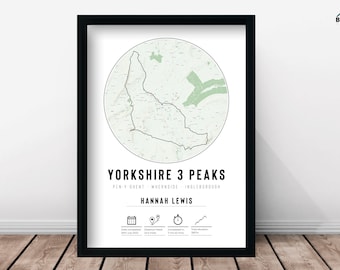 May include: A black framed print featuring a green and white map of the Yorkshire Three Peaks trail. The text "Yorkshire 3 Peaks" is at the top of the print, followed by the names of the peaks: "Pen-y-ghent", "Whernside", and "Ingleborough". The name "Hannah Lewis" is below the peak names. The print also includes icons for the date the trail was completed, the distance, the time, and the total elevation gain.