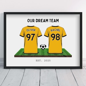 May include: Framed print showing two yellow and black football shirts with the names "Oliver" and "Rachel" and numbers 97 and 98. A football sits between the shirts on a green pitch. The text "OUR DREAM TEAM" and "EST. 2025" are displayed.