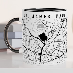May include: White ceramic mug with a black rim and handle. The mug features a black and white map of St. James' Park with the text "St. James' Park" printed on the side.