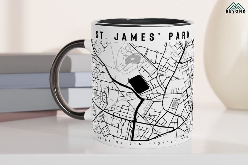 May include: White ceramic mug with a black rim and handle. The mug features a black and white map of St. James' Park with the text "St. James' Park" printed on the side.