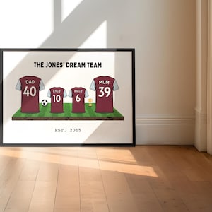 May include: Framed print featuring a family's soccer jerseys on a green field. The jerseys are maroon with white sleeves and include the names and numbers of each family member. The text "THE JONES' DREAM TEAM" and "EST. 2015" are also displayed.