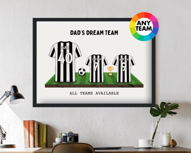 May include: A framed print featuring three soccer jerseys with black and white stripes, a soccer ball, and a trophy on a green field. The text reads "DAD'S DREAM TEAM" and "ALL TEAMS AVAILABLE". A color wheel graphic is in the upper right corner.
