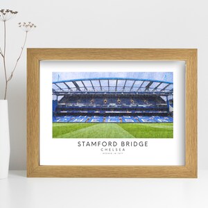 May include: A framed print of Stamford Bridge, the home of Chelsea Football Club in London, England. The print features a watercolor-style illustration of the stadium with the text "Stamford Bridge, Chelsea, London, England" below the image.