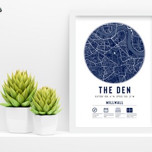 Pu&ograve; includere: Una stampa incorniciata bianca con una mappa blu di Millwall, Londra, Inghilterra. La mappa &egrave; in un cerchio con il testo "THE DEN" e le coordinate "51&deg;29'09.4"N 0&deg;03'03.2"W". Il testo "MILLWALL" &egrave; sotto le coordinate.