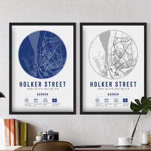 May include: Two framed prints of a map of Holker Street in Barrow, England. The map is in a circle with a blue background on the left and a grey background on the right. The prints are black framed and have the coordinates and name of the street printed below the map.