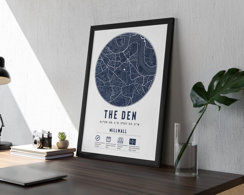 Pu&ograve; includere: Una stampa incorniciata nera con una mappa blu navy di Millwall, Londra. La stampa ha il titolo "The Den" e le coordinate "51&deg;29' 08.4" N 0&deg;03' 03.2" W".