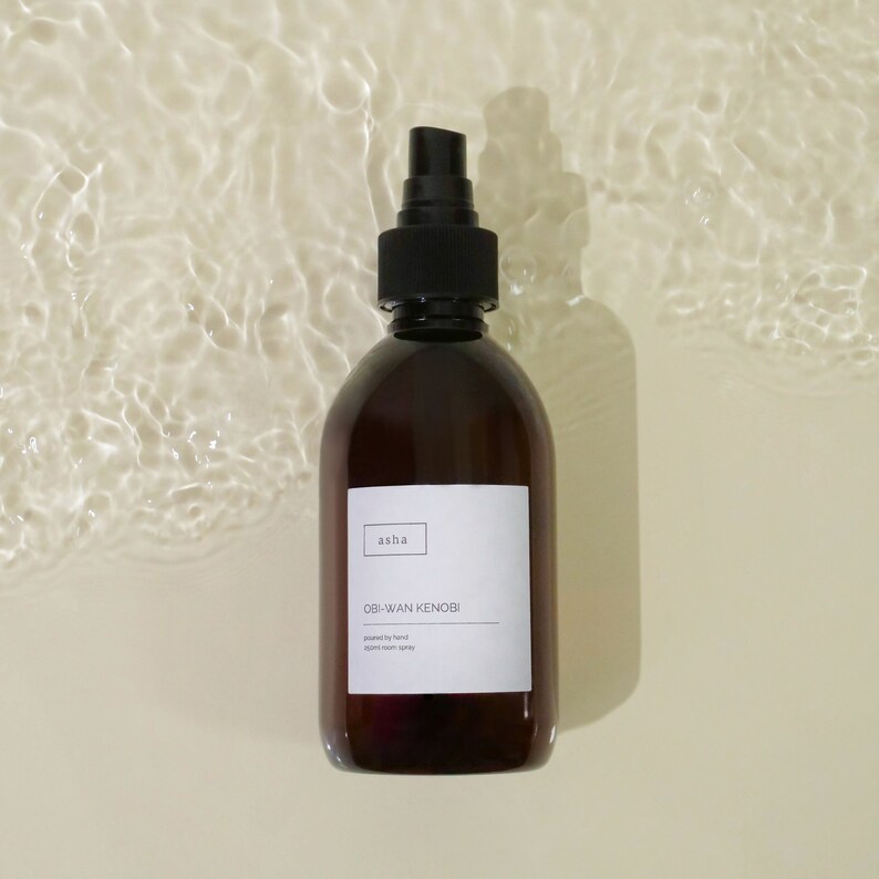 Pu&ograve; includere: Un flacone di vetro marrone con un ugello spray nero. Il flacone ha un'etichetta bianca con il testo "asha" e "OBI-WAN KENOBI" stampato su di essa. L'etichetta dice anche "powered by hand" e "ambient room spray".