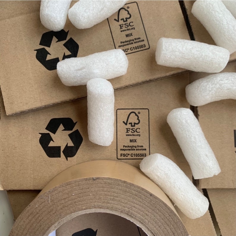Pu&ograve; includere: Primo piano di un rotolo di nastro adesivo marrone con noccioline di polistirolo bianco sparse intorno. Il nastro ha un nucleo di cartone marrone ed &egrave; etichettato con il logo FSC e il testo: "FSC www.fsc.org MIX Packaging from responsible sources FSC C105503".
