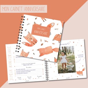 以下が含まれることがあります： オレンジ色のキツネのイラストと「MON CARNET ANNIVERSAIRE」の文字が描かれた白い表紙のリング綴じバースデーメモリーブック。中ページには、誕生日詳細用の罫線、子供の写真、キツネのグラフィックが印刷されています。