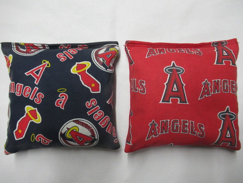 May include: Two square bean bags. One is navy blue with red and white Angels logos and text. The other is red with white Angels logos and text. Both are filled and ready for play.