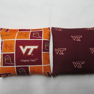 May include: Two bean bags with a Virginia Tech logo. One bean bag is orange and maroon with the VT logo and a Hokie bird. The other bean bag is maroon with the VT logo repeated.
