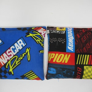 May include: Two blue and black fabric bean bags with NASCAR logos and designs. The bean bags are square shaped and have a variety of colors and patterns.