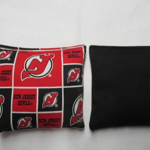 May include: Two bean bags, one with a black and red checkered pattern featuring the New Jersey Devils logo, and one solid black bean bag.