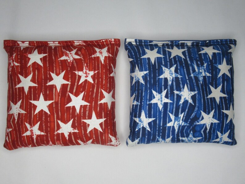 May include: Two bean bags with a red and blue star pattern. The bean bags are made of fabric and have a white background with red and blue stripes.