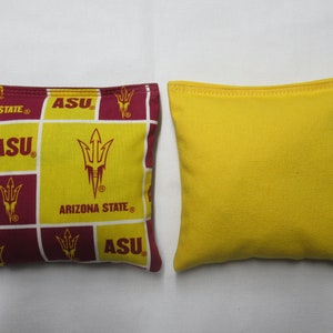 May include: Two bean bags for a game of cornhole. One bean bag is yellow and the other is maroon with a repeating pattern of the Arizona State University logo, the letters "ASU", and the words "Arizona State".