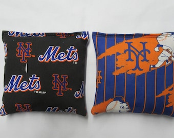 Puede incluir: Dos bolsas de frijoles con el logotipo de los New York Mets. Una bolsa de frijoles es negra con el logotipo de los Mets y las palabras "Mets" en azul y naranja. La otra bolsa de frijoles es azul con rayas naranjas y blancas y el logotipo de los Mets en naranja.