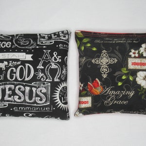 May include: Two decorative square pillows. One black pillow features white text including "Peace", "Messiah", "Lamb of God", and "Jesus". The other black pillow has a cross, flowers, and the words "Amazing Grace".