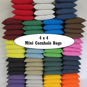 May include: A set of 16 mini cornhole bags in various colors, including red, white, blue, green, brown, yellow, black, beige, purple, orange, and pink. The bags are stacked in rows of four, with the text "4 x 4 Mini Cornhole Bags" displayed in a white oval in the center of the image.