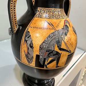 May include: Black and orange Greek amphora with two handles, a black and white painted scene of a warrior and a woman, and the text "EXSEKIASEMOIESE" and "?O3VIXA".