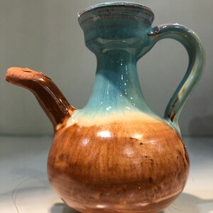 May include: A brown and blue ceramic pitcher with a spout and a handle. The pitcher has a glazed finish and a rounded body.
