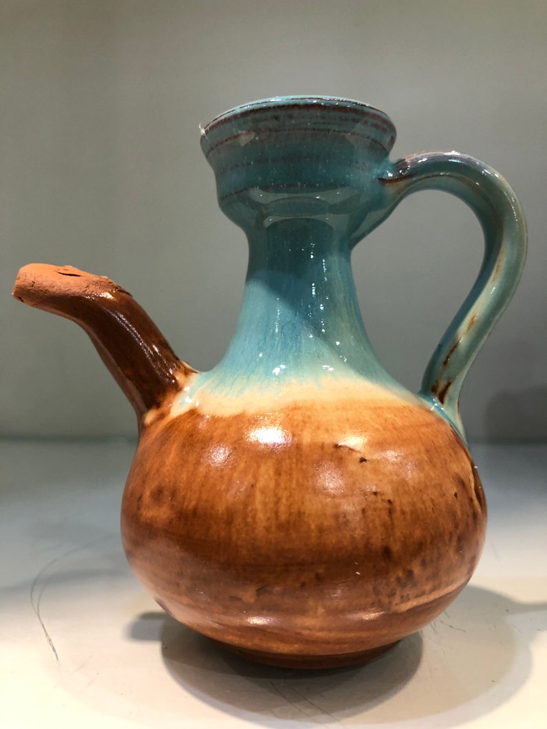 May include: A brown and blue ceramic pitcher with a spout and a handle. The pitcher has a glazed finish and a rounded body.