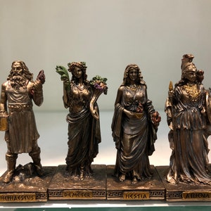 May include: Set of five bronze Greek goddess figurines, each standing on a base with their name inscribed in Greek. The goddesses are Hephaestus, Demeter, Hestia, and Athena.