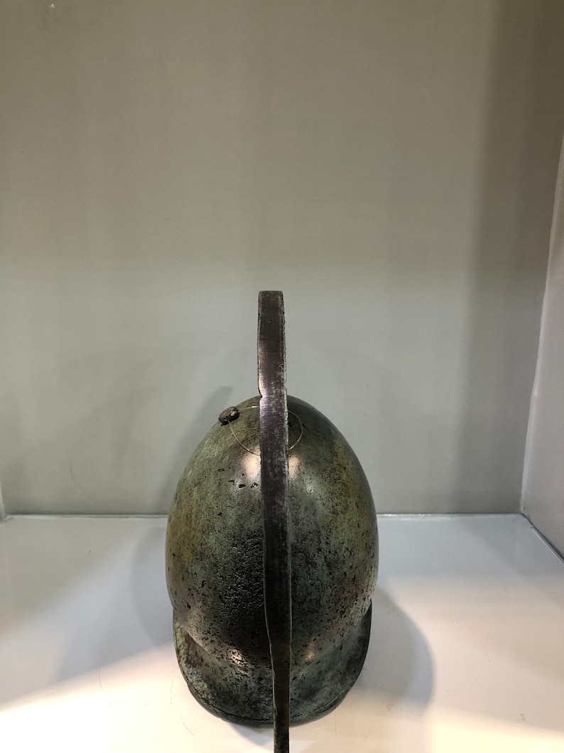 May include: A bronze helmet with a long, curved crest. The helmet is green and has a textured surface.