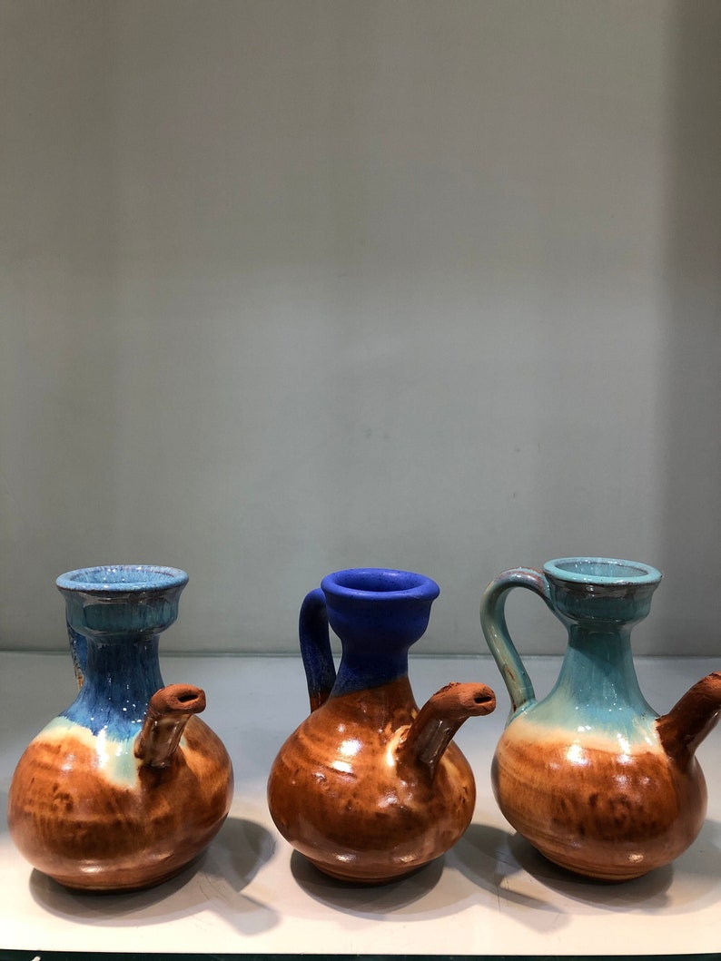 May include: Three ceramic jugs with brown, blue, and green glaze. The jugs have a rounded body and a spout on the side.
