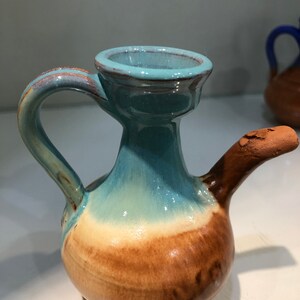 May include: A small, ceramic pitcher with a light blue glaze and a brown base. The pitcher has a handle and a spout.