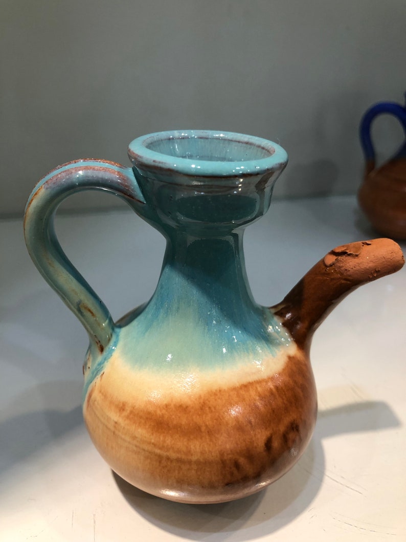 May include: A small, ceramic pitcher with a light blue glaze and a brown base. The pitcher has a handle and a spout.