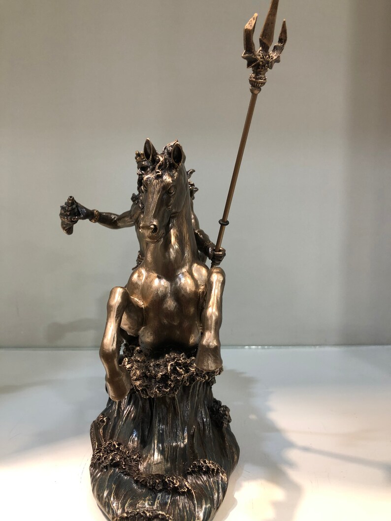 K&ouml;nnte beinhalten: Bronzefarbene Statue einer Figur auf einem Pferd, die aus stilisierten Wellen auftaucht. Die Figur h&auml;lt einen Dreizack und ein kleines Objekt. Die Statue ist detailliert und scheint eine mythologische oder historische Darstellung zu sein.
