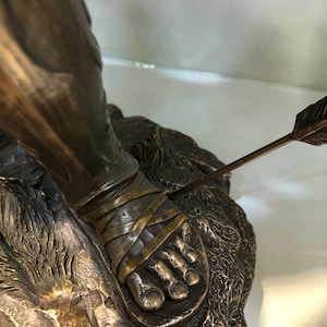 May include: Bronze sculpture of a man with an arrow through his foot. The sculpture is detailed and shows the man's foot bound with straps.