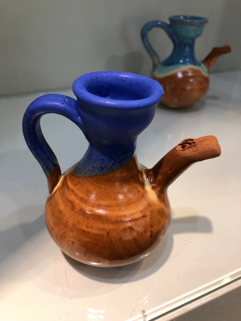 May include: Two small ceramic pitchers with brown and blue glaze. The pitcher on the left has a blue spout and a brown handle. The pitcher on the right has a blue spout and a brown handle.