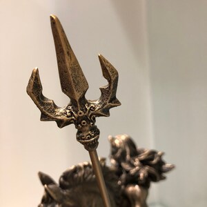 K&ouml;nnte beinhalten: Bronzestatue einer Figur auf einem Pferd, die einen Dreizack h&auml;lt. Der Dreizack hat drei Zinken und aufwendige Details. Die Statue hat ein verwittertes Aussehen, das auf einen antiken Stil hindeutet. Auch das Haar der Figur und die M&auml;hne des Pferdes sind detailliert.