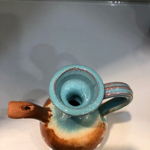 May include: A small, brown and blue ceramic pitcher with a spout and a handle. The pitcher has a glazed finish and a unique, swirling pattern.
