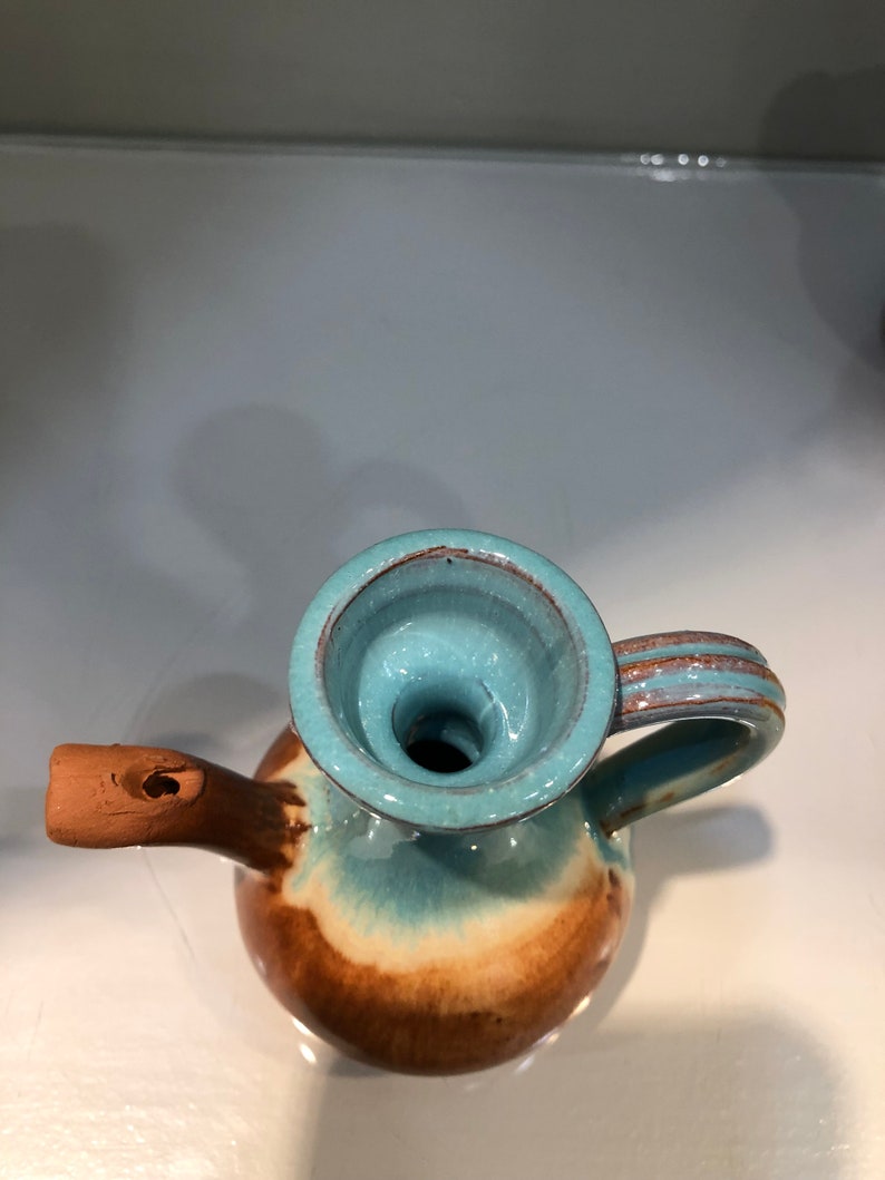 May include: A small, brown and blue ceramic pitcher with a spout and a handle. The pitcher has a glazed finish and a unique, swirling pattern.