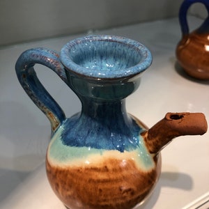 May include: A small, blue and brown ceramic pitcher with a handle and a spout. The pitcher has a glazed finish and a rounded body.