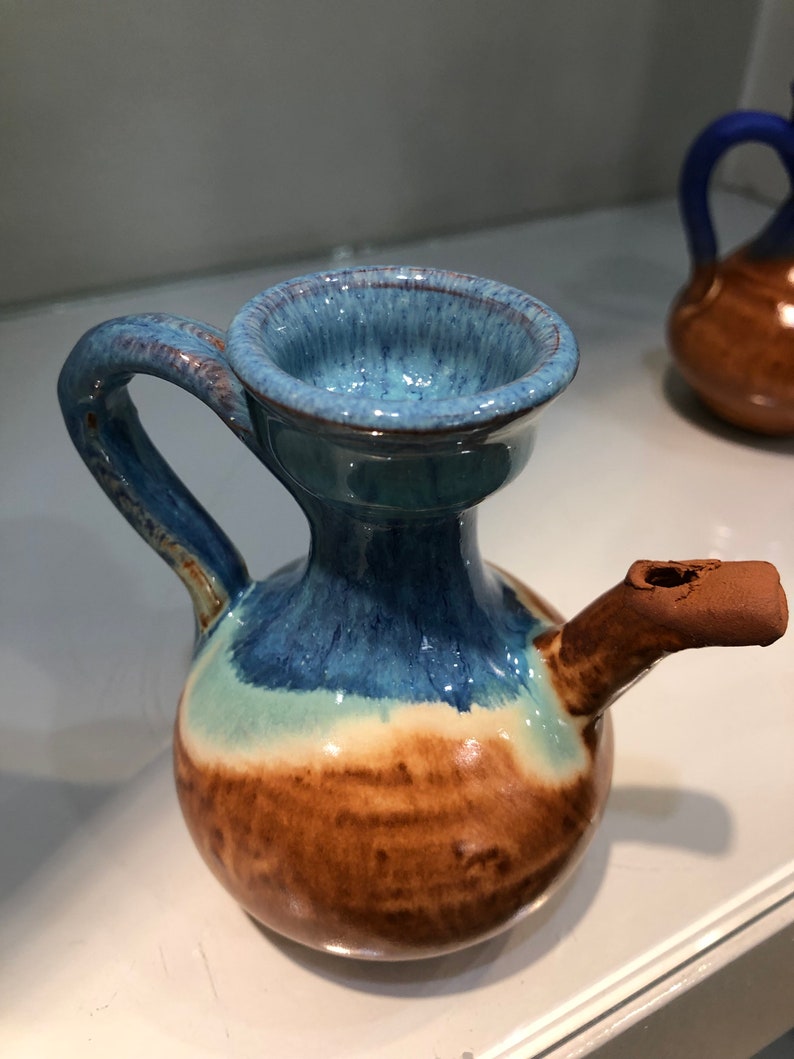 May include: A small, blue and brown ceramic pitcher with a handle and a spout. The pitcher has a glazed finish and a rounded body.