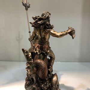 K&ouml;nnte beinhalten: Bronzefarbene Statue einer mythologischen Figur, die einen Dreizack und einen abgetrennten Kopf h&auml;lt. Die Figur hat lange Haare und sitzt auf einem Seeungeheuer. Die Statue ist detailliert und steht auf einem Sockel, der Meereswellen darstellt.